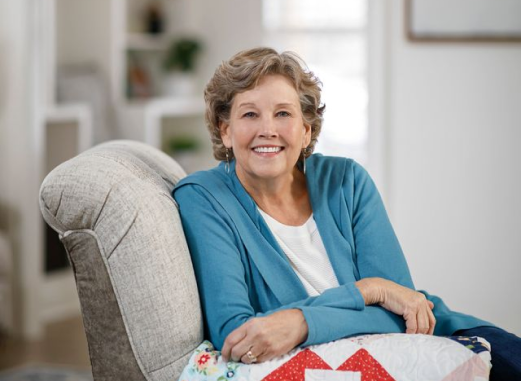 Jenny Doan sitting on a chair with a quilt